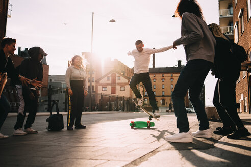 Männliche und weibliche Freunde betrachten einen jungen Mann, der in der Stadt einen Stunt auf dem Skateboard macht - MASF11399