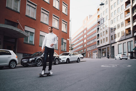 In voller Länge von jungen Mann Skateboarding auf der Straße gegen Gebäude in der Stadt, lizenzfreies Stockfoto