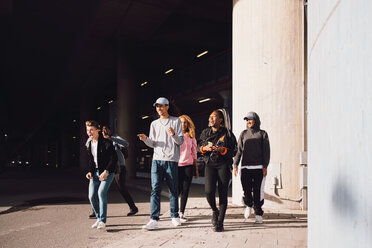 Happy friends looking away while walking on street under overpass in city during sunny day - MASF11412