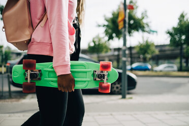 Mittelteil einer jungen Frau, die ein grünes Skateboard hält, während sie in der Stadt spazieren geht - MASF11419