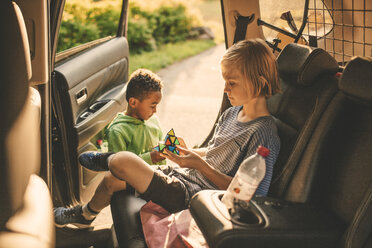 Mädchen spielt Puzzle-Würfel, während sie im Auto neben ihrem Bruder im Park sitzt - MASF11433