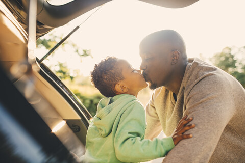 Vater küsst Sohn, der im Kofferraum eines Autos sitzt, lizenzfreies Stockfoto