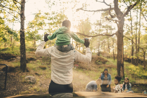 Mann trägt Sohn beim Picknick mit der Familie im öffentlichen Park auf den Schultern - MASF11440