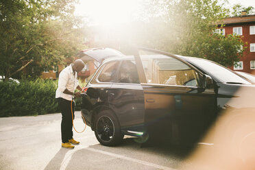 Full length of man charging electric car on driveway - MASF11448