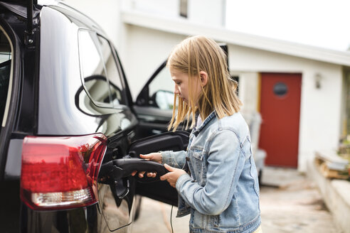 Seitenansicht eines blonden Mädchens, das ein Elektroauto in einer Einfahrt auflädt - MASF11474