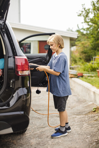 Seitenansicht eines Mädchens, das ein Elektroauto in der Einfahrt auflädt, lizenzfreies Stockfoto