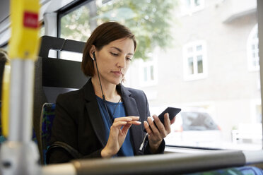 Mittelgroßer weiblicher Pendler, der im Bus sitzend sein Smartphone benutzt - MASF11485