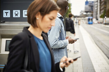 Pendler benutzen ihr Smartphone, während sie auf dem Bürgersteig in der Stadt warten - MASF11486