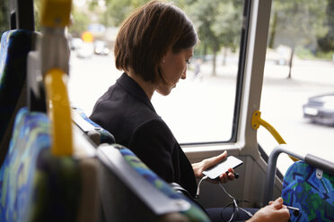 Mittlere erwachsene Geschäftsfrau, die ein Smartphone benutzt, während sie im Bus sitzt - MASF11490