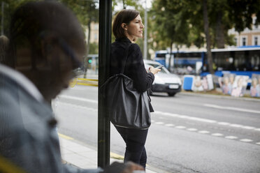 Geschäftsfrau schaut weg, während sie an der Bushaltestelle mit einem Pendler in der Stadt steht - MASF11491