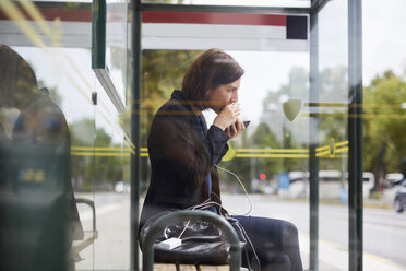 Seitenansicht einer Geschäftsfrau, die ein Sandwich isst, während sie an einer Bushaltestelle in der Stadt wartet - MASF11498