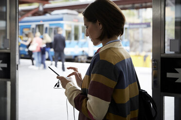 Geschäftsfrau, die ein Smartphone benutzt, während sie im Bahnhof steht - MASF11499