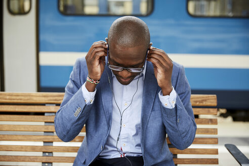 Geschäftsmann passt In-Ear-Kopfhörer an, während er am Bahnhof sitzt - MASF11500