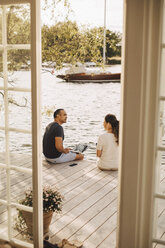 Älteres Paar, das sich bei der Arbeit auf der Terrasse unterhält, gesehen durch die offene Tür einer Ferienvilla - MASF11509
