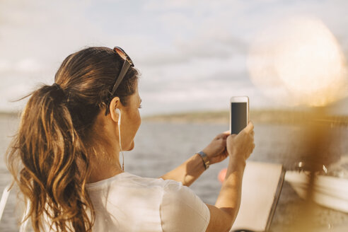 Frau nimmt Selfie durch Handy gegen See während des Sommerurlaubs - MASF11512
