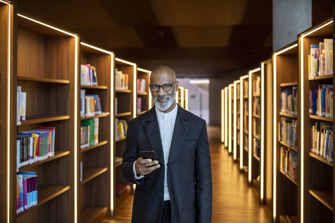 Portrait of smiling businessman with smartphone at library stock photo