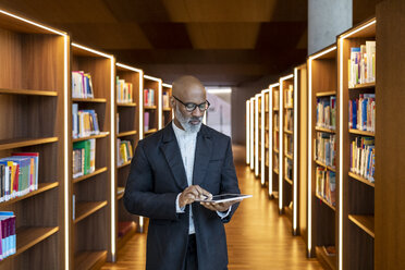 Mature businessman using digital tablet at library - FMKF05352