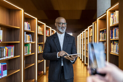 Porträt eines lächelnden Geschäftsmannes mit digitalem Tablet in einer Bibliothek - FMKF05353