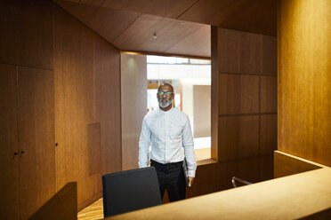 Porträt eines reifen Mannes mit Laptop an einem Arbeitsbereich mit Holzverkleidung - FMKF05358