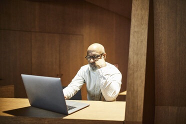 Porträt eines reifen Mannes, der an einem Arbeitsplatz mit Holzverkleidung an einem Laptop arbeitet - FMKF05359