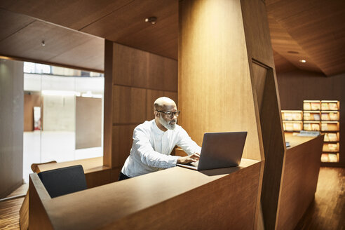 Älterer Mann arbeitet am Laptop an einem Arbeitsplatz in einer Bibliothek - FMKF05360