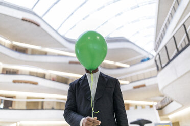 Mature businessman hiding face behind green balloon - FMKF05365