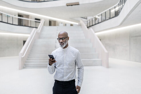Portrait of mature businessman standing at foyer looking at cell phone - FMKF05370