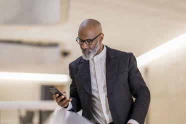 Porträt eines glatzköpfigen reifen Geschäftsmannes, der auf sein Mobiltelefon schaut - FMKF05399