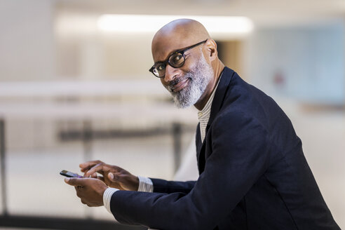 Portrait of smiling mature businessman with cell phone - FMKF05400