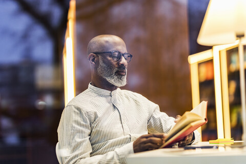 Porträt eines Mannes, der abends in der Bibliothek ein Buch liest, lizenzfreies Stockfoto