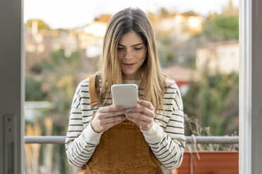 Portrait of young woman standing on balcony looking at cell phone - AFVF02394