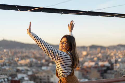 Porträt einer glücklichen jungen Frau, die sich bei Sonnenuntergang auf einer Dachterrasse entspannt, lizenzfreies Stockfoto