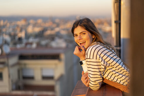 Porträt einer lachenden jungen Frau auf einem Balkon bei Sonnenuntergang - AFVF02417