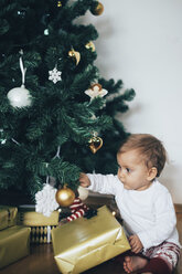 Kleines Mädchen sitzt auf dem Boden und spielt mit Weihnachtsschmuck - MOMF00627