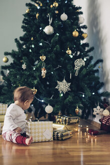 Kleines Mädchen sitzt auf dem Boden und spielt mit Weihnachtsgeschenken - MOMF00628