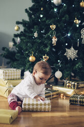 Kleines Mädchen sitzt auf dem Boden und packt Weihnachtsgeschenke aus - MOMF00629