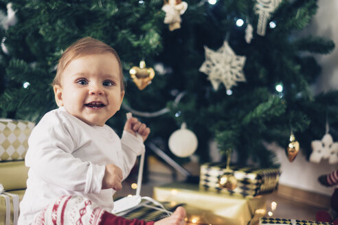 Porträt eines lächelnden kleinen Mädchens beim Auspacken von Weihnachtsgeschenken - MOMF00630