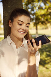 Lächelnde junge Frau, die ihr Smartphone in einem Park benutzt - JHAF00036