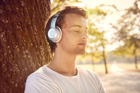 Junger Mann mit Kopfhörern, der draußen Musik hört, lizenzfreies Stockfoto