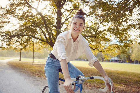Porträt einer lächelnden jungen Frau, die in einem Park Fahrrad fährt, lizenzfreies Stockfoto