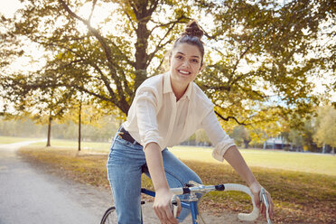 Portrait of smiling young woman riding bike at a park - JHAF00047