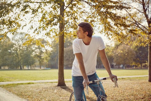 Junger Mann mit Fahrrad im Park schaut sich um - JHAF00051