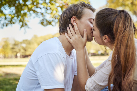 Junges verliebtes Paar küsst sich in einem Park, lizenzfreies Stockfoto