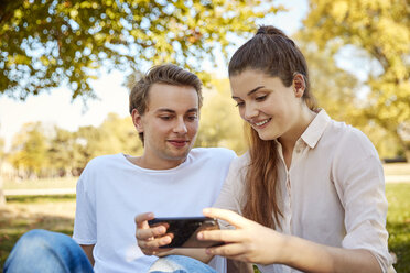 Junges Paar schaut in einem Park auf sein Smartphone - JHAF00063