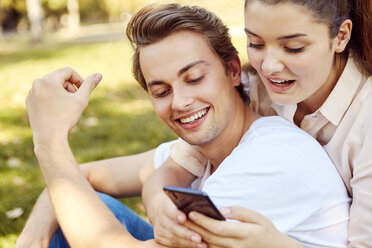 Young couple looking at smartphone at a park - JHAF00067