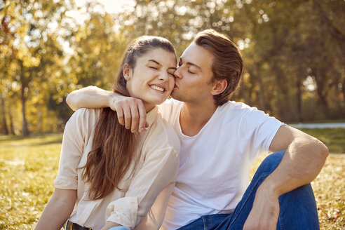 Glückliches junges Paar, das sich in einem Park küsst - JHAF00070
