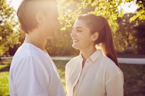 Junges Paar lächelt sich in einem Park bei Sonnenuntergang an, lizenzfreies Stockfoto