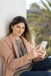 Porträt einer lächelnden jungen Frau, die ein Mobiltelefon hält - AFVF02429