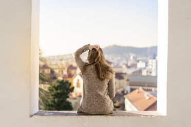 Rückansicht einer jungen Frau, die auf einer Mauer sitzt - AFVF02430