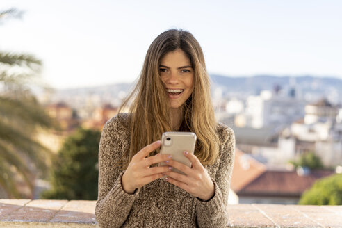 Porträt einer lachenden jungen Frau mit Handy in der Hand - AFVF02434